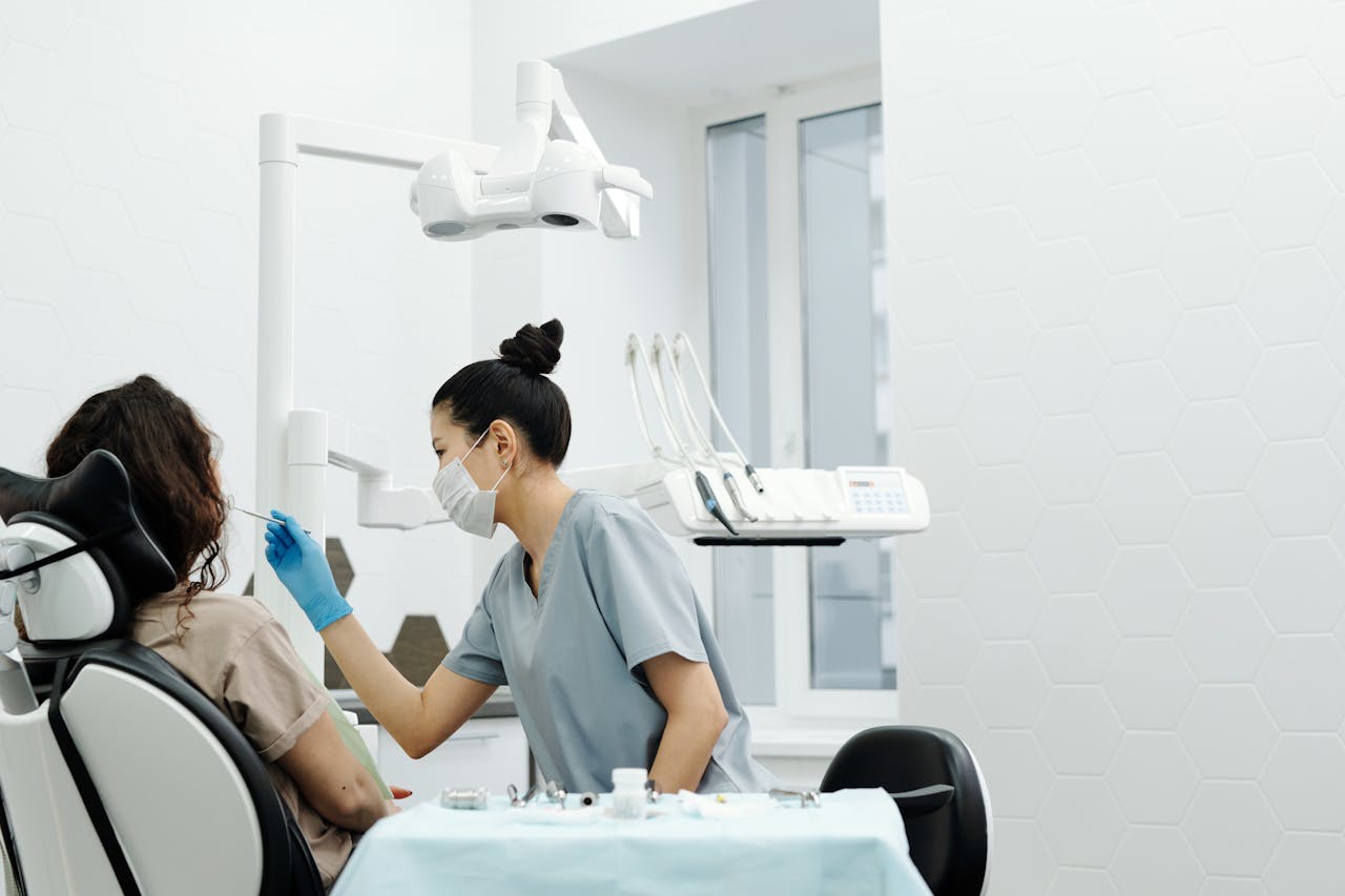 A dentist wearing protective gear examines a patient in a modern clinic setting.
